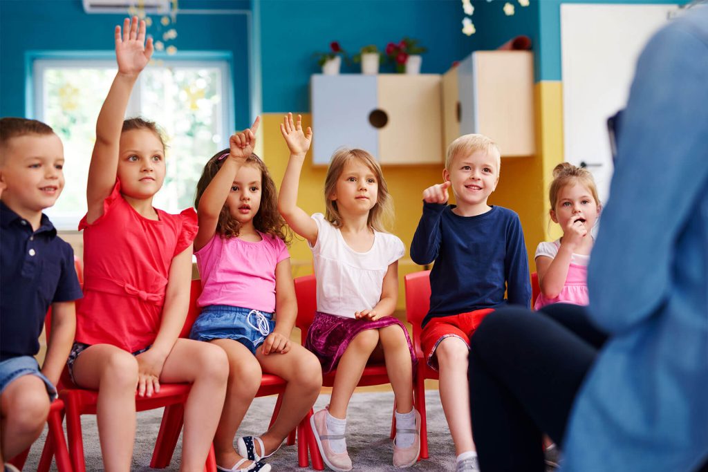 kids sitting down and raising their hands to answer a question