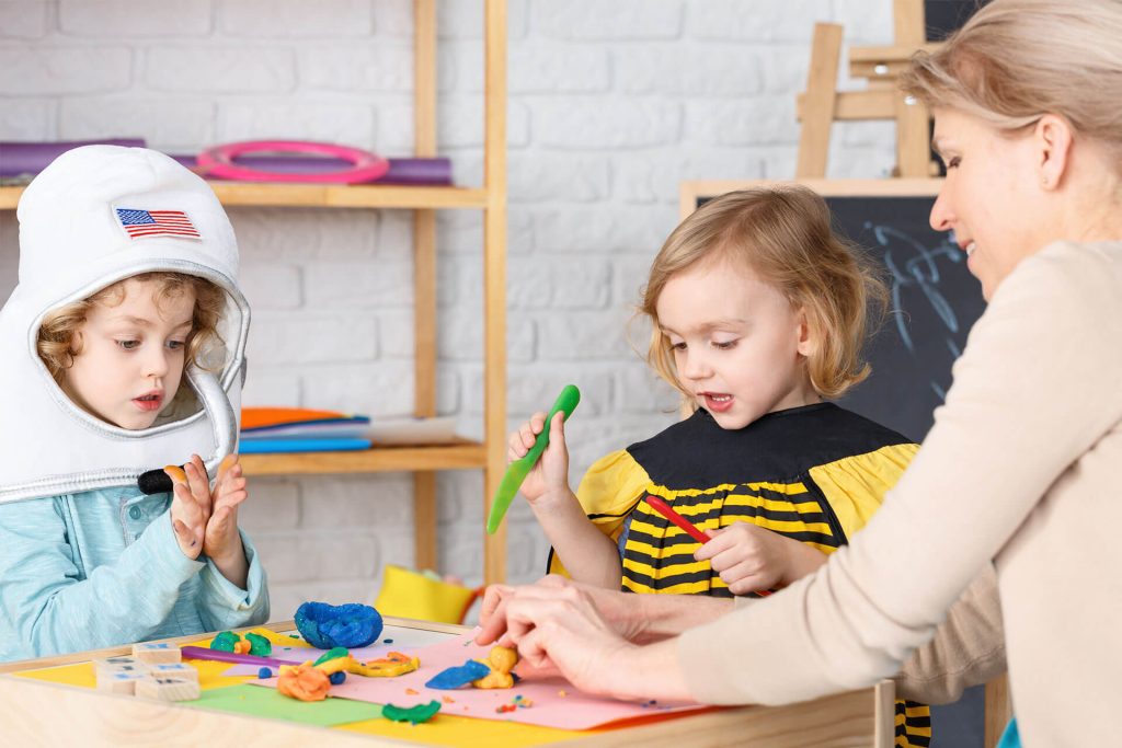 adult woman playing with playdoh with two young boys